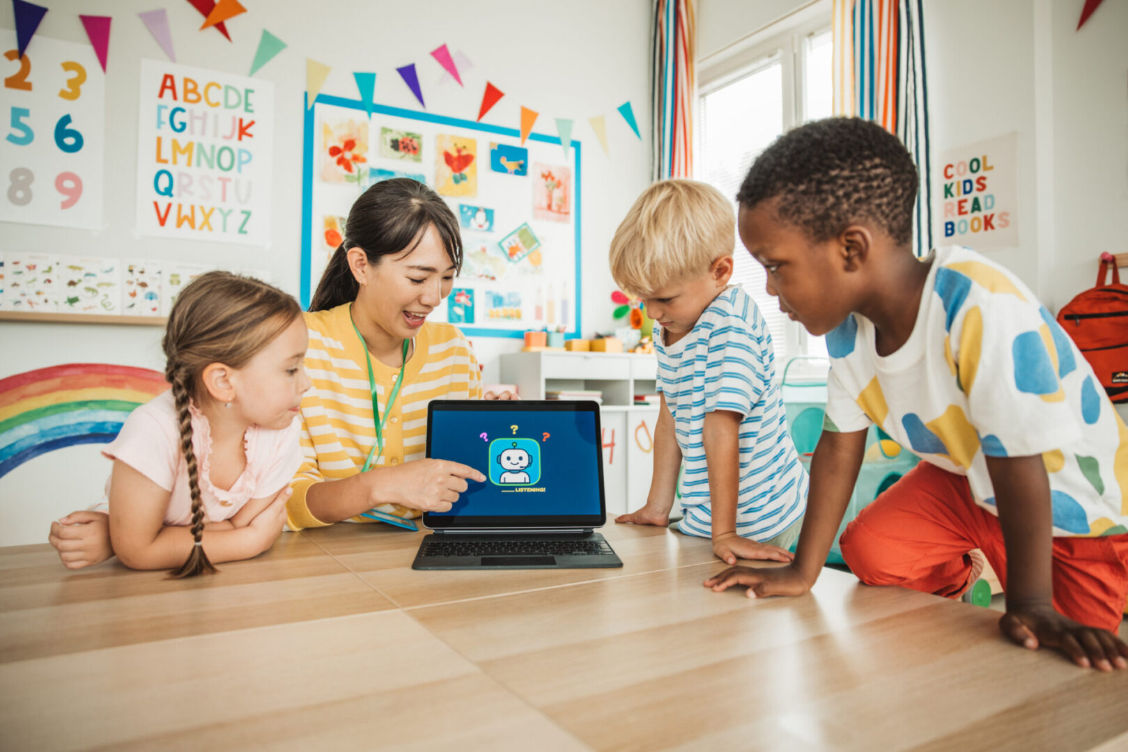 Female teacher is surrounded by her kindergarten students as she shows them how to use a robot on digital tablet.